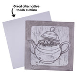Carved lino block and smooth tile displayed side by side with annotation text reading Great alternative to silk cut lino. The carved block shows a mouse inside a teapot with vertical background lines, while the blank light-grey tile sits slightly behind.