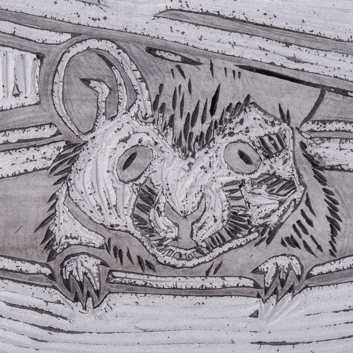 Macro close-up of the carved lino tile surface showing the mouses face and paws emerging from the teapot. Recessed gouge marks form fur texture and contour lines. Fine carved grooves and speckled residue are visible within the cut areas.