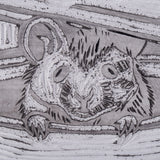 Macro close-up of the carved lino tile surface showing the mouses face and paws emerging from the teapot. Recessed gouge marks form fur texture and contour lines. Fine carved grooves and speckled residue are visible within the cut areas.