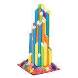 Tall architectural tower sculpture constructed from vibrant coloured ECO Paper Straws in blue, orange, yellow, green and pink, arranged in vertical columns with diamond-shaped cutouts. The structure stands on a square cardboard base decorated with multicoloured mosaic paper squares in rainbow hues.