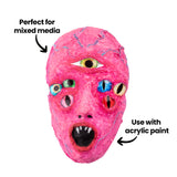 Bright pink plaster mask with multiple inset eyes and painted details. Annotations read “Perfect for mixed media” and “Use with acrylic paint,” highlighting compatibility with paint and collage materials.