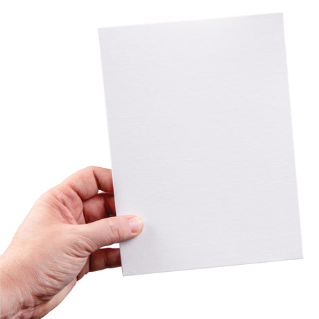 A hand holds a small rectangular canvas board against a light background. The white primed canvas surface shows a subtle woven texture across the board, with clean straight edges and a rigid backing.