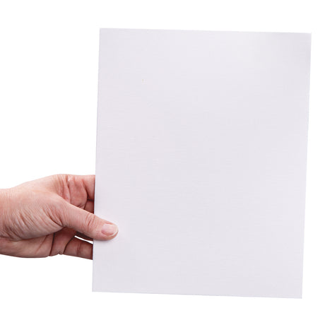 A hand holds a square white canvas board. The primed canvas surface shows a fine fabric weave across the entire board, with a rigid flat backing visible along the edges.
