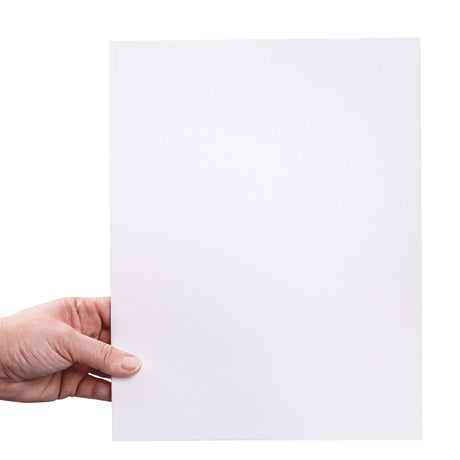 A hand holds a large canvas board upright against a pale background. The white primed canvas surface shows a fine woven texture across the board, suitable for painting and mixed media. The board appears thin with firm straight edges.