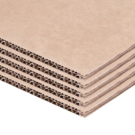 A stack of brown Backdrop Card sheets is photographed from an angled close-up view, highlighting the corrugated fluted core between smooth kraft paper layers. The layered cardboard edges create repeating linear textures, showing the material’s strength, thickness and structural quality for construction and craft applications.