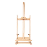 Front view of a natural wood tabletop easel with a slim vertical frame, adjustable centre support and horizontal canvas ledge. The easel is photographed against a light grey background, showing visible woodgrain texture, brass fittings and a compact rectangular base with clean symmetrical lines.