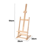 Natural wood tabletop easel displayed at an angle against a light grey background with black dotted measurement annotations reading 54cm, 29cm and 32cm. The easel features visible woodgrain texture, brass fittings, adjustable centre support and a compact rectangular base with clean geometric lines.
