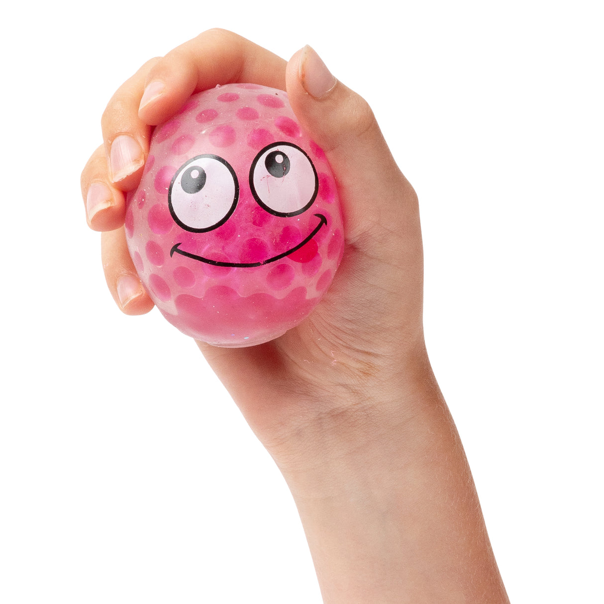A child's hand squeezes a translucent pink stress ball filled with gel beads, decorated with a smiling face featuring large cartoon eyes and a cheerful grin. The squishy sensory toy demonstrates the tactile, squeezable nature of the EmotiBalls, showing how the gel beads create texture beneath the stretchy surface.