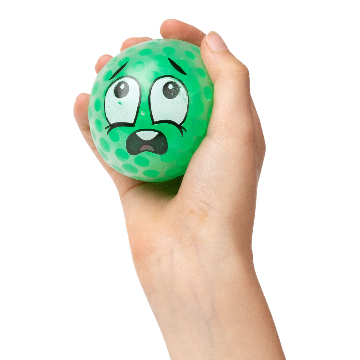 A child's hand squeezes a bright green textured foam ball decorated with a worried facial expression featuring wide eyes, raised eyebrows, and an open mouth. The squishy sensory ball has darker green spots across its dimpled surface, demonstrating the tactile and expressive qualities of the EmotiBalls.