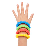 Child's hand and wrist wearing four brightly coloured textured fidget bracelets in blue, green, coral, and yellow. Each Sensory Sprouts bracelet features a raised bumpy surface pattern, stacked together on the wrist against a white background, demonstrating their sensory tactile qualities.