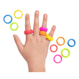 Child's hand wearing four colourful textured fidget rings in red, pink, orange and yellow on different fingers, surrounded by eight additional rings in blue, green, pink, orange and coral featuring varied tactile surfaces including smooth bands and spiky gear-like edges from the Sensory Sprouts Textured Fidget Rings set.