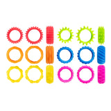 Set of twelve colourful textured fidget rings arranged in three rows, displaying six different tactile patterns including spiked gears, smooth rings, scalloped edges, and ribbed surfaces in bright red, lime green, orange, blue, yellow, and magenta plastic.