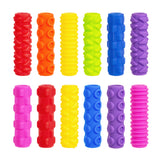 Twelve brightly coloured cylindrical pencil grips arranged in two rows, each featuring distinct tactile patterns including waves, circles, zigzags, dots, and ridges. The Sensory Sprouts grips come in vibrant red, orange, yellow, lime green, blue, purple, and pink finishes.