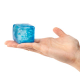 A hand holds a translucent blue jelly cube with marbled swirls of lighter and darker blue throughout. The Sensory Sprouts Jelly Cube has a glossy, smooth surface with visible texture variations. The cube is approximately palm-sized, demonstrating its soft, squishy sensory properties. The white background highlights the vibrant ocean-like colours within the tactile toy.