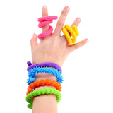 Child's hand displaying six flexible textured silicone strings in bright colours including pink, yellow, purple, blue, orange and green. Each twistable string features different tactile surfaces - smooth spirals, ribbed patterns and spiky textures - worn as bracelets around the wrist and twisted around individual fingers for sensory play and fidgeting.