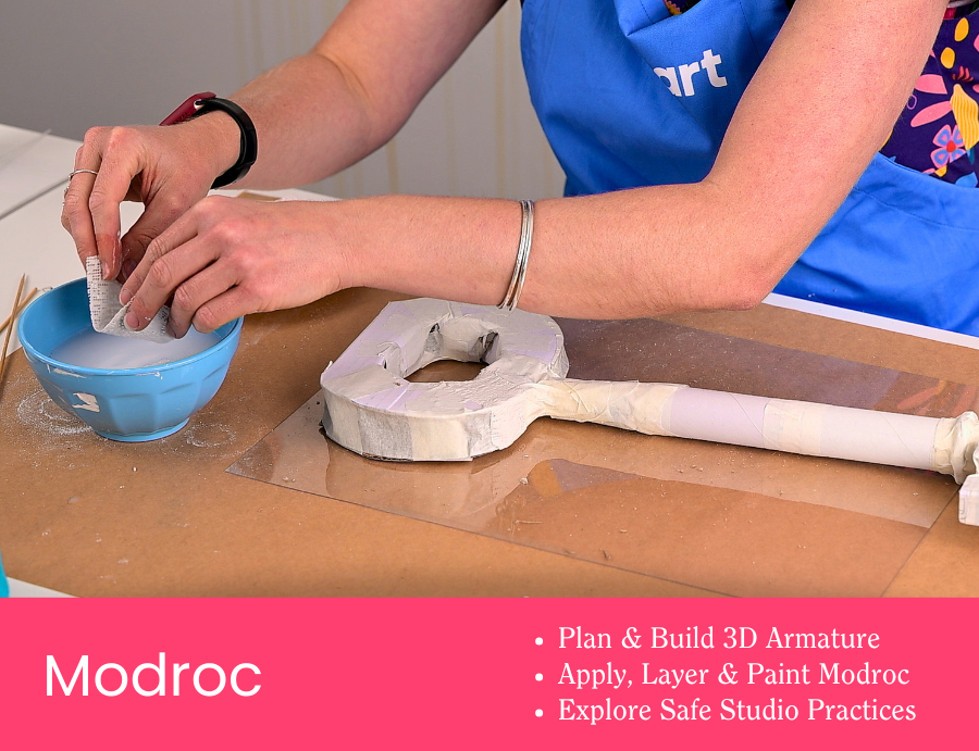 Workshop tile showing hands dipping Modroc strips into a blue bowl beside a partially built armature structure wrapped in tape and paper. The workspace includes a long cardboard tube and a plastic-covered table surface. Pink banner text reads “Modroc” with dot points: “Plan & Build 3D Armature”, “Apply, Layer & Paint Modroc”, “Explore Safe Studio Practices”. Credit: Zart Education PL The Essentials of Modelling.