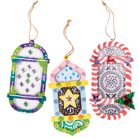 Three decorated Zart Wooden Lantern Frames hang side by side on jute string. The left is painted purple and green with silver and green gem clusters; the centre features a pink and blue onion-dome shape with a yellow star and sequins; the right shows red-and-white stripes with a silver embossed medallion and holly.