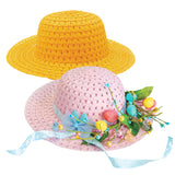 Two woven straw hats in bright yellow and pastel pink. The pink Easter Bonnet Straw Hat 29cm is decorated with colourful spring embellishments including blue fabric flowers, green leaves, decorative eggs in turquoise, coral and yellow, and flowing light blue ribbon ties at the brim.