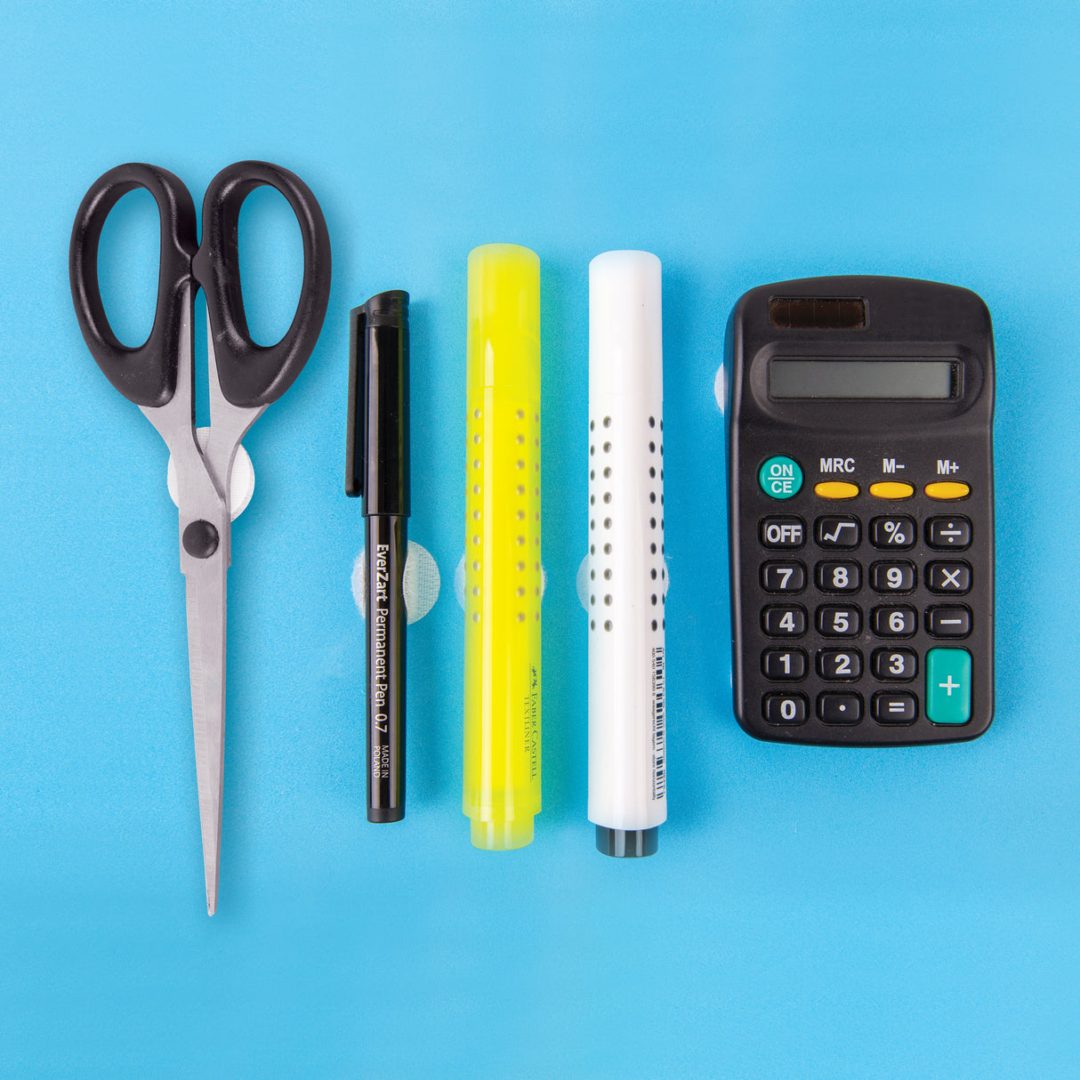Flat lay of scissors, black pen, bright yellow highlighter, white marker and black calculator arranged on a light blue background, each item attached with small white circular hook fastener dots visible beneath them.
