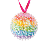 Zart Pearl Headed Pins, densely inserted into a round ball to form a rainbow-coloured sequinned bauble, transitioning through pink, orange, yellow, green, blue and purple. White pearl heads cover the surface in tight rows, with a pink ribbon loop at the top for hanging.