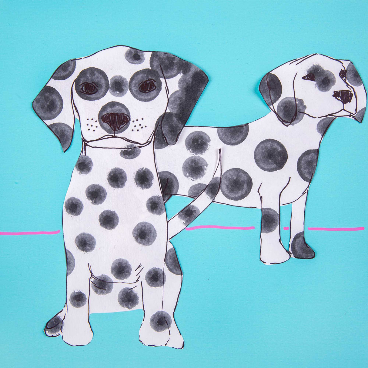 Two paper dog cut-outs decorated with stamped black dots on a bright blue background. The spots vary in size and opacity, showing layered sponge stamping effects.