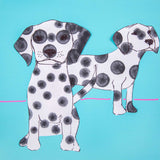 Two paper dog cut-outs decorated with stamped black dots on a bright blue background. The spots vary in size and opacity, showing layered sponge stamping effects.