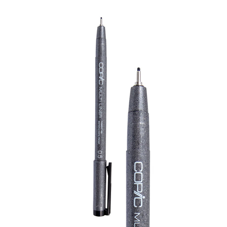 A Copic Multi Liner fineliner pen with a 0.5mm nib, shown uncapped alongside a close-up of the tip. The dark grey speckled barrel displays white "COPIC MULTI LINER" lettering and a black clip on the cap. The metal-collared nib extends to a slightly broader black point.