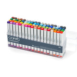 A clear plastic case holding Copic Classic alcohol markers arranged in rows. White barrels with grey ends and coloured caps show a wide colour range, each labelled with alphanumeric codes. Front label reads “COPIC classic,” “72 colours set A,”