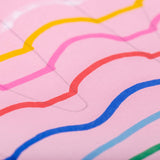 Close-up view of bright curved lines drawn with POSCA paint markers on pink paper, showing smooth opaque strokes in yellow, pink, red, blue and green.