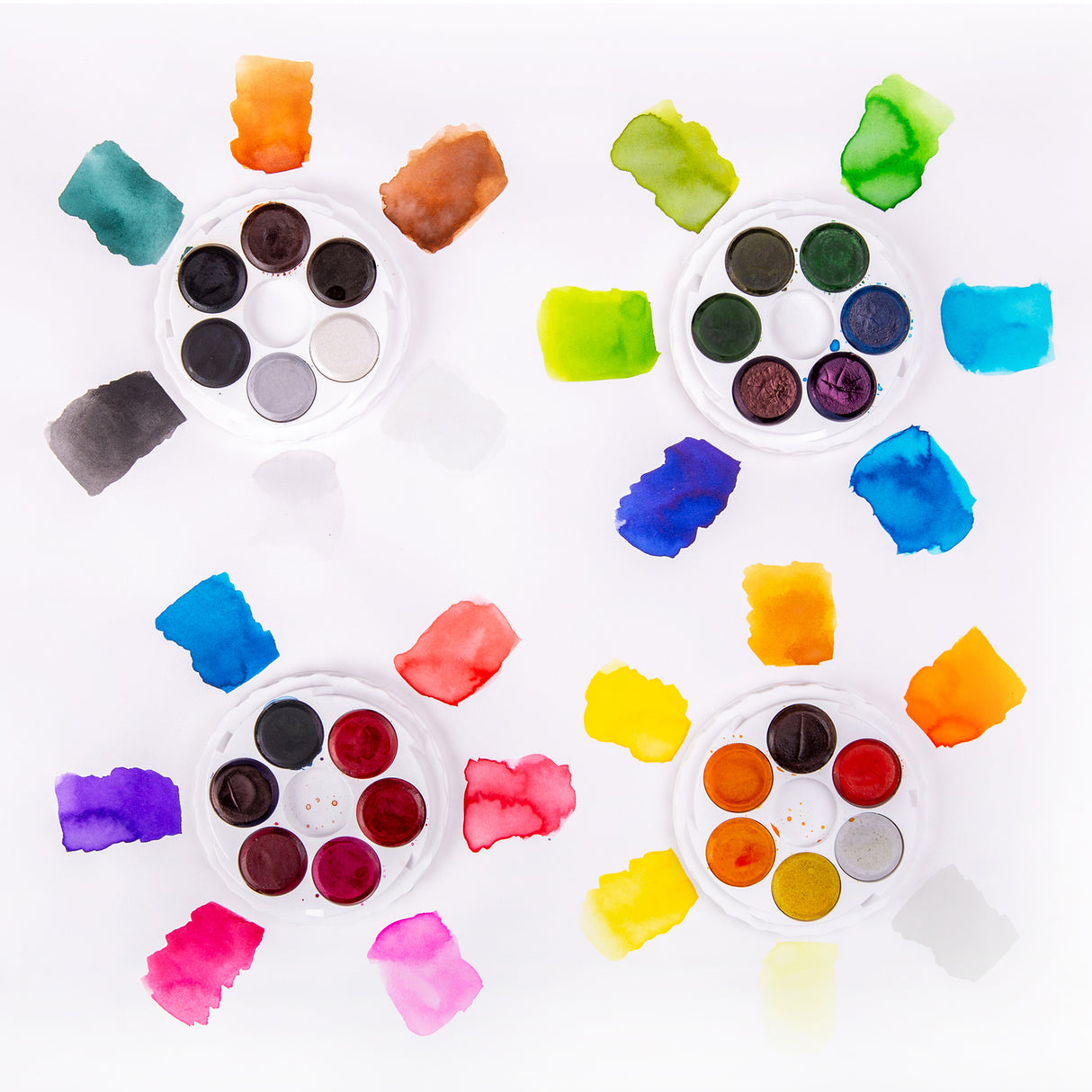 Four open round Micador Brilliant Water Colours discs are surrounded by painted swatches on white paper. Colours include greys, browns, greens, blues, yellows, oranges, reds, pinks and purples, with soft wash effects, feathered edges and varying pigment density.