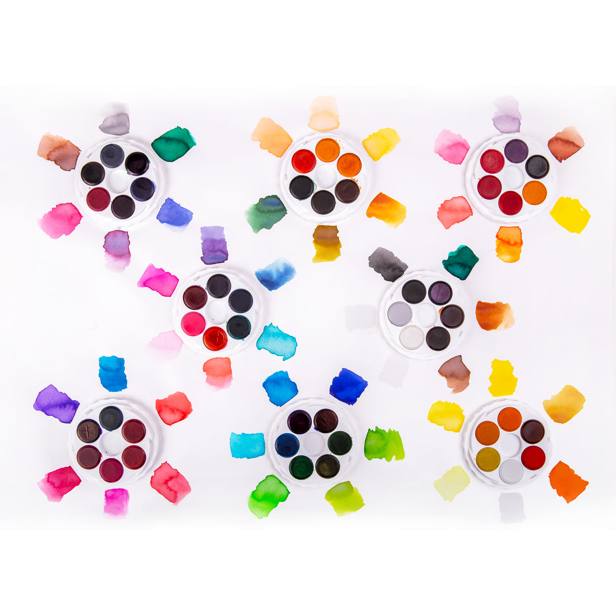 Six open Micador Brilliant Watercolours discs are arranged on white paper, each surrounded by loose painted swatches. Colours include yellows, oranges, reds, pinks, purples, blues, greens, greys and browns, with watery gradients, uneven edges and pigment blooms.