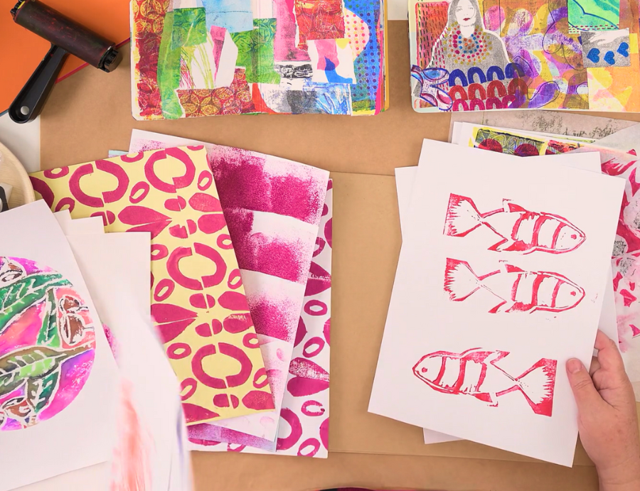 Zart Education PL The Essentials of Printing – A top-down view of colourful printmaking materials and student samples, including hand-printed fish motifs in red ink, vibrant gel-plate prints, patterned papers in pink and yellow, and collage artworks, with an artist’s hands holding a sheet of freshly printed fish designs.