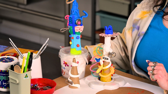 A workshop table displaying three works-in-progress from the Zart Education On Demand lesson Lost Thing Sculpture Inspired By Shaun Tan, presented by Francesca Spillane. Each sculpture is built over a cardboard cone or roll using Creative Clay (air dry paper clay), with embedded buckles, chenille stems, beads and coloured clay details reflecting the Industrial Retro aesthetic of Shaun Tan's creatures.